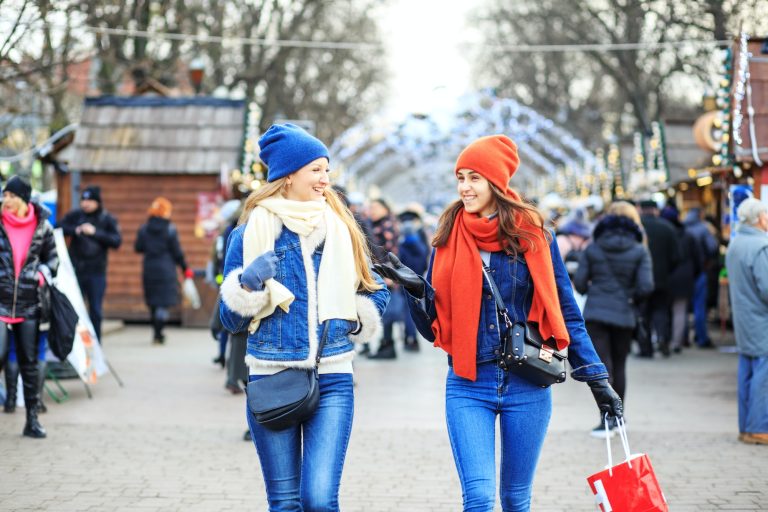 Two young girls met at the Christmas market and are walking. Women communicate and buy gifts.